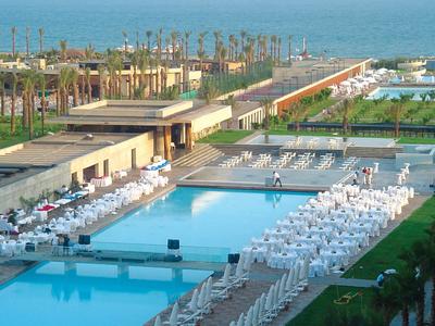 Espace piscine d'hôtel avec chaises longues blanches et vue sur la mer et les palmiers.