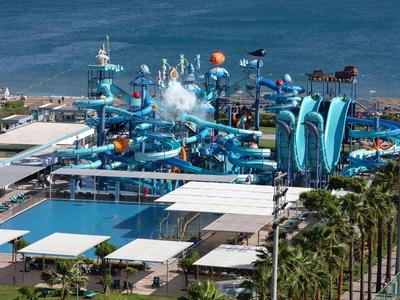 Parc aquatique avec toboggans et piscine en bord de mer, entouré de palmiers et de zones de détente.