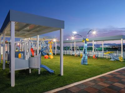 Aire de jeux avec toboggans et balançoires à côté d'un chemin pavé au crépuscule.