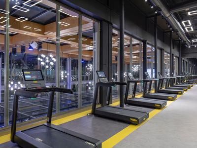 Salle de sport moderne avec plusieurs tapis de course devant de grandes fenêtres et sol gris