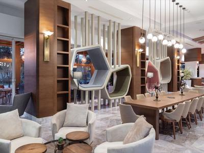 Espace salon d'hôtel moderne avec des fauteuils confortables et de longues tables en bois.