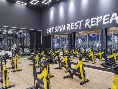 Modern gym with yellow spin bikes, dark walls, and light wooden flooring.