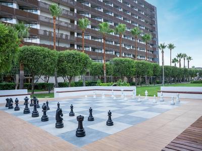 Large outdoor chessboard in front of a hotel with green areas and palm trees.