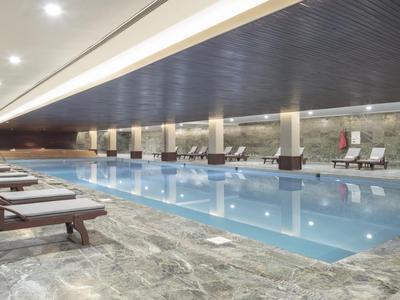 Modern indoor pool with lounge chairs and stylish lighting in a hotel.