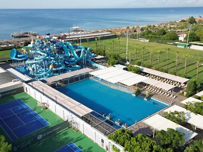 Large pool with blue water slides and sports courts near the sea.