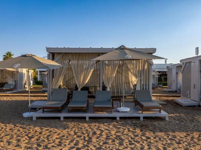 Four sun loungers with large umbrellas and white daybeds on sandy beach.