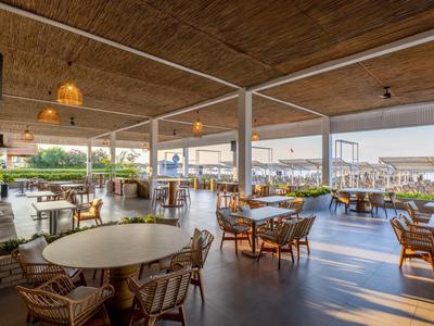 Open dining area with wooden ceilings and cozy chairs in a hotel by the water.