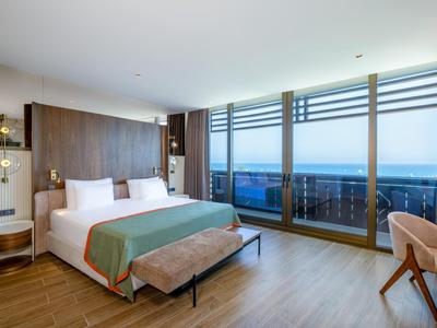 Modern hotel room with large bed and panoramic windows overlooking the sea.