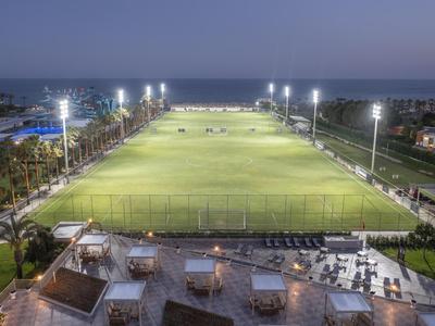 Illuminated sports field with adjacent seating areas and sea view at dusk.