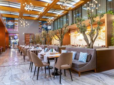 Modern hotel dining area with wooden ceiling, plants, and elegant seating.