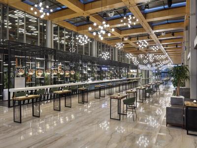 Modern hotel lobby area with long tables, stools, and bright lighting.