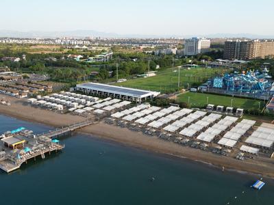 Aerial view of a busy beach with white umbrellas and a pier extending into the water.