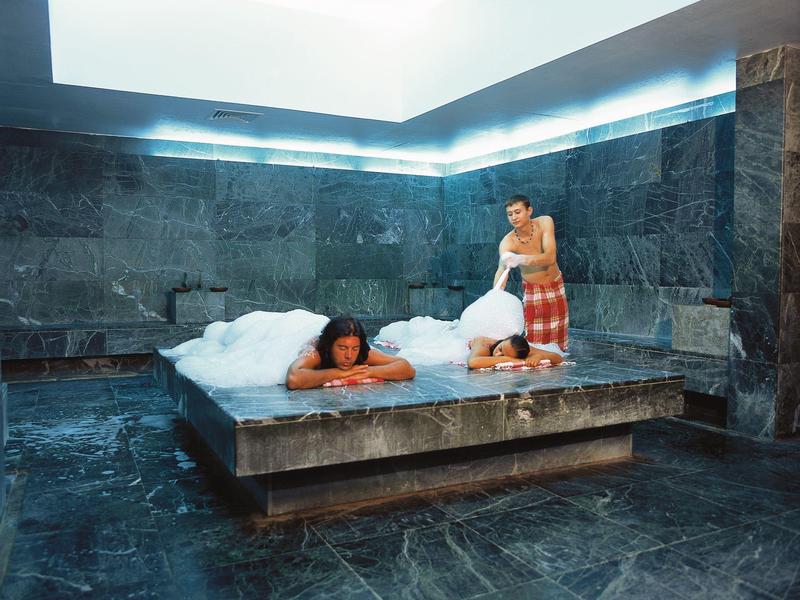 Personne se détend sur un lit en pierre couvert de mousse dans un hammam moderne.