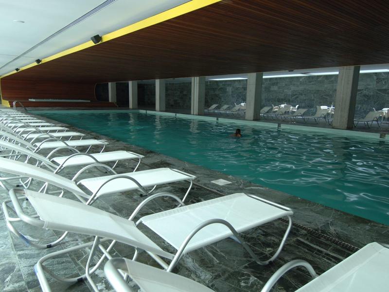 Piscine intérieure avec rangées de chaises longues blanches et grandes fenêtres
