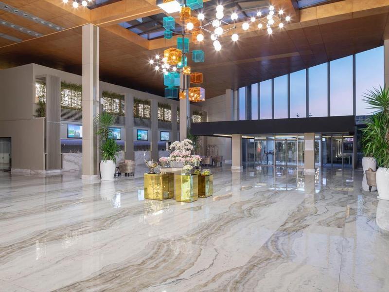 Hall d'hôtel moderne avec sol en marbre, grandes fenêtres et lustres colorés.