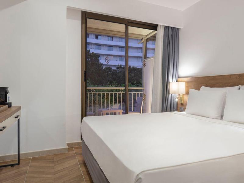 Chambre d'hôtel moderne avec lit double, télévision à écran plat et balcon offrant une vue sur le coucher de soleil.