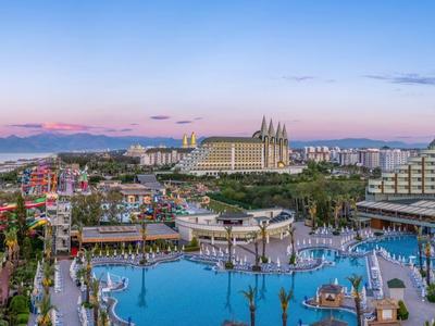 Panoramisch uitzicht op een luxe resort met zwembaden en Middellandse Zee op de achtergrond bij zonsondergang.
