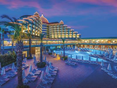 Hotel con area piscina illuminata e lettini al crepuscolo sotto un cielo colorato.