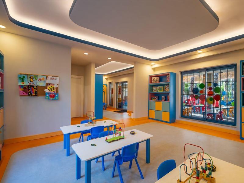 Heldere kinder speelkamer met tafels, stoelen, kleurrijke wandkasten en kunst aan muren.