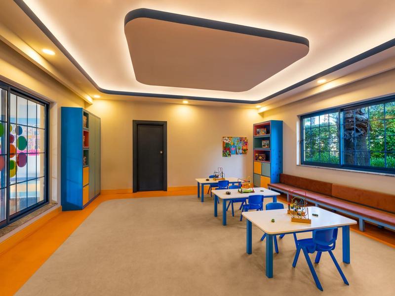 Lichte klas met kleurrijke stoelen, een groot raam en speelse muurschilderingen in een hotel.