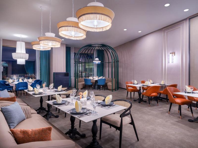 Modern hotelrestaurant met stijlvolle verlichting en tafelopstelling in warme kleuren.