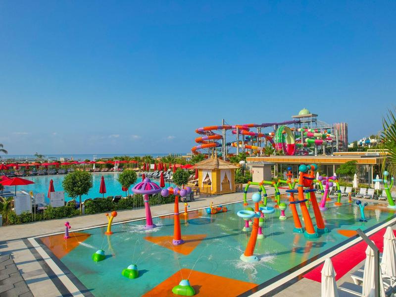 Kleurrijk waterpark met glijbanen en waterspelletjes onder blauwe lucht.