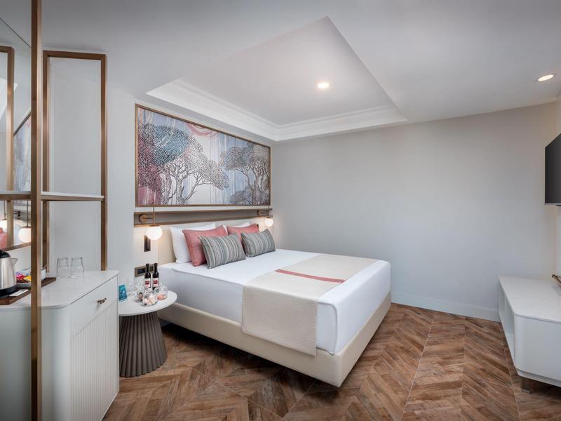 Moderne hotelkamer met tweepersoonsbed, wandkunst, tv en houten vloer in neutrale tinten.