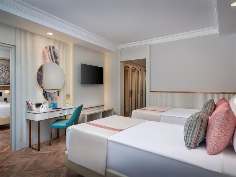 Tweepersoonskamer met modern meubilair, bureau, tv en badkamer op de achtergrond.