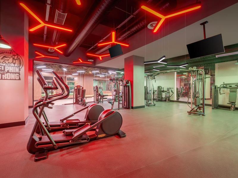 Fitnessruimte met moderne apparatuur en rode plafondverlichting in een hotel.