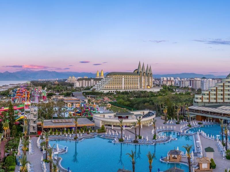 Panoramisch uitzicht op een luxe resort met zwembaden en Middellandse Zee op de achtergrond bij zonsondergang.