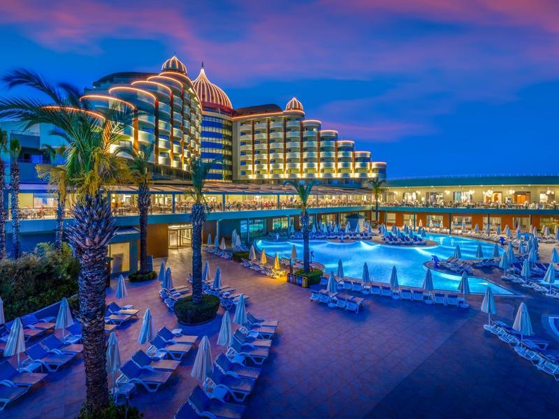 Luxe hotel met verlicht zwembad en ligstoelen bij zonsondergang.