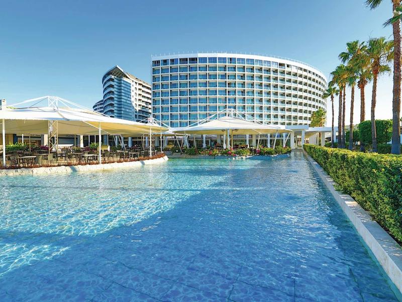 Complejo hotelero moderno con gran piscina y palmeras bajo un cielo despejado.