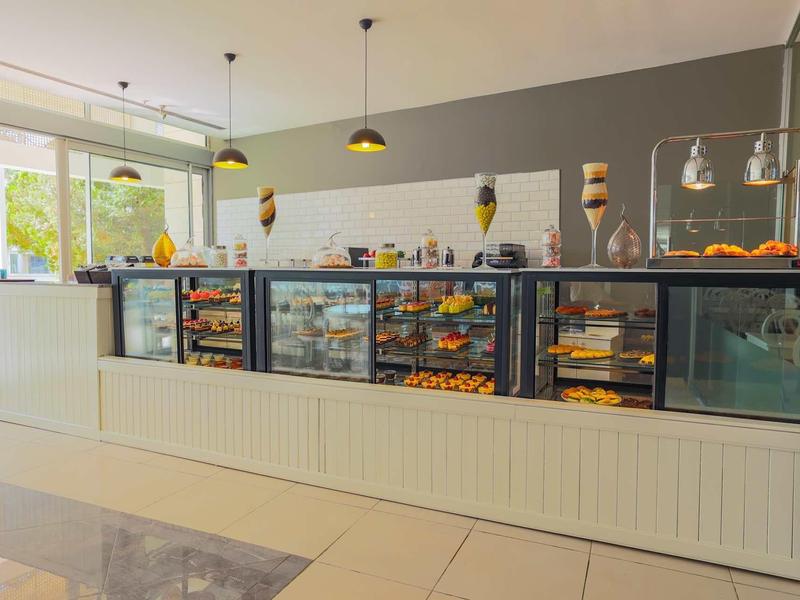 Mostrador moderno de café con vitrina de cristal, selección de pasteles y asientos en espacio luminoso.