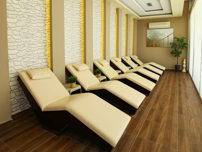 Fila de cómodas tumbonas en una sala de spa moderna con suelo de madera y grandes ventanas.