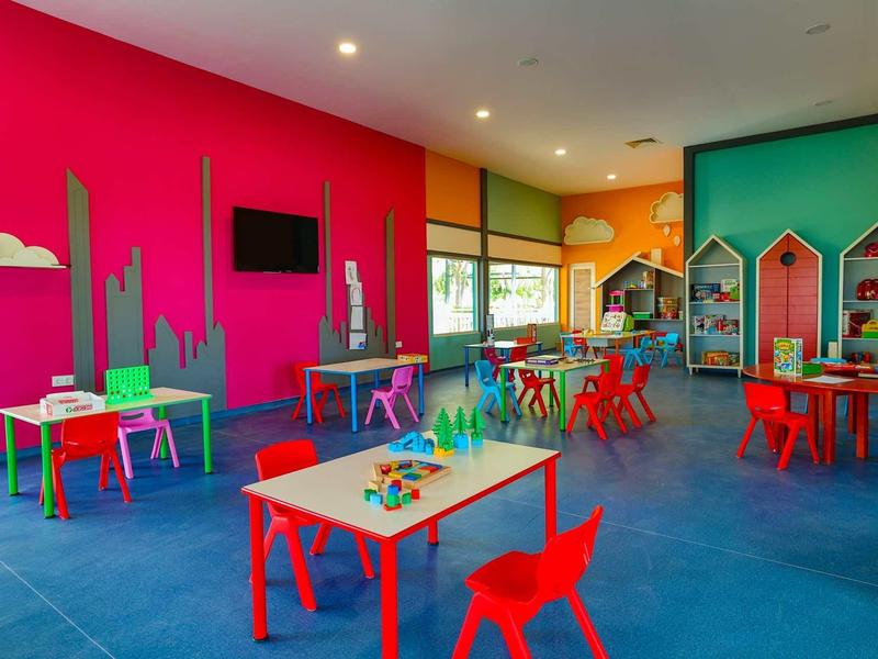 Sala infantil colorida con pequeñas mesas y sillas, juguetes y paredes coloridas.
