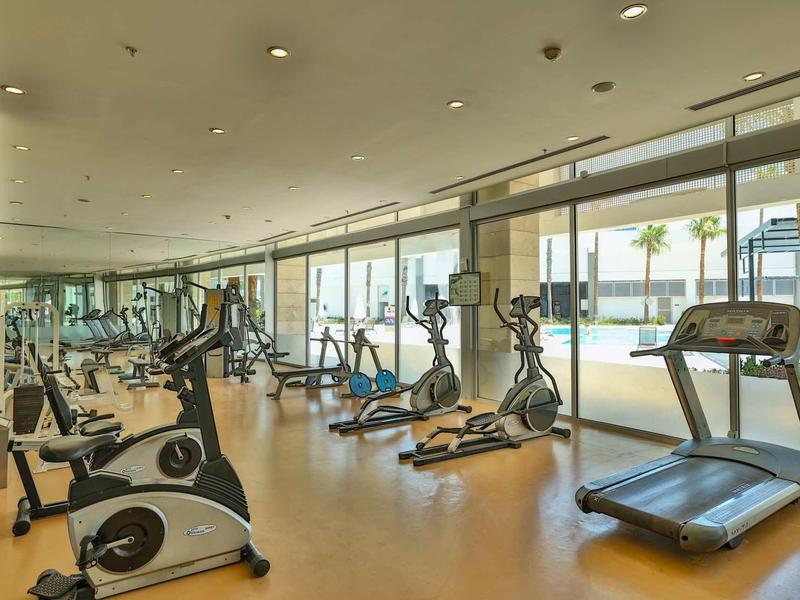 Sala de fitness moderna con bicicletas estáticas, elípticas y cintas de correr junto a grandes ventanas.