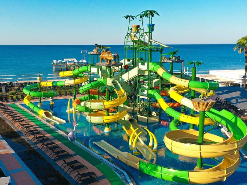 Toboganes de agua coloridos y piscinas en un parque acuático junto al mar bajo un cielo despejado.