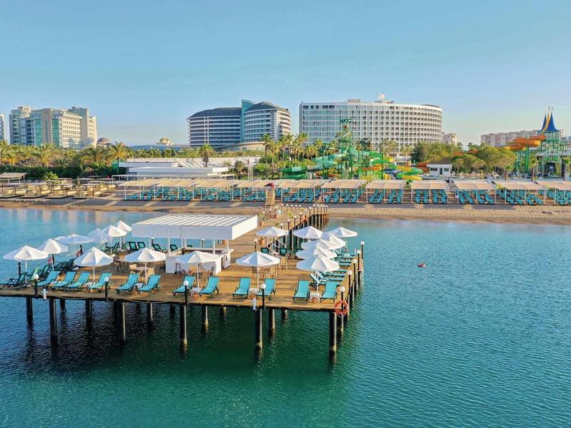Muelle con tumbonas y sombrillas frente a un hotel junto al mar bajo un cielo despejado.