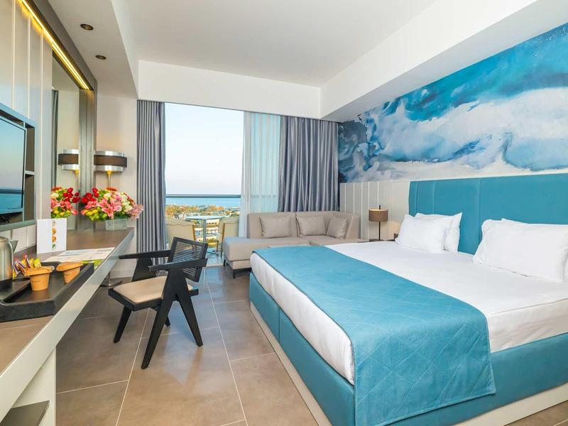 Habitación de hotel moderna con cama grande, vista al mar y área de estar acogedora.