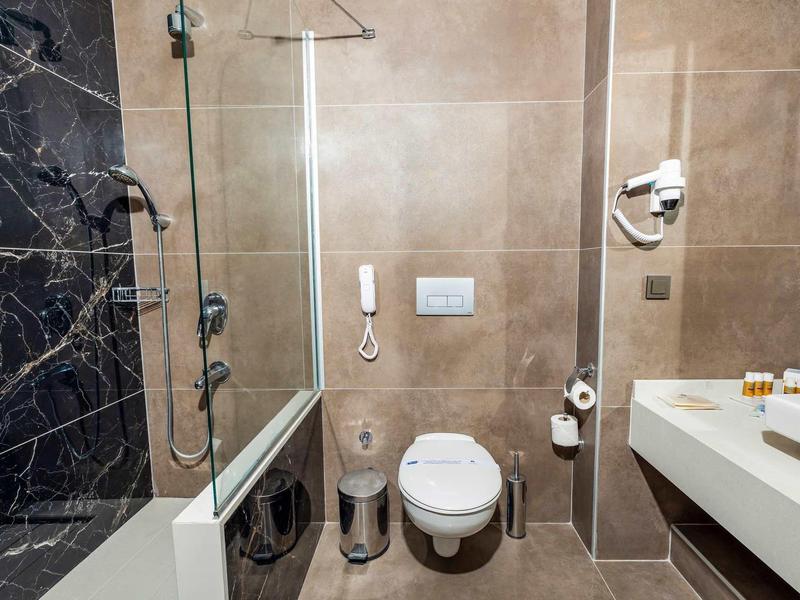 Baño moderno con inodoro, ducha, lavabo y secador de pelo en una habitación de hotel.