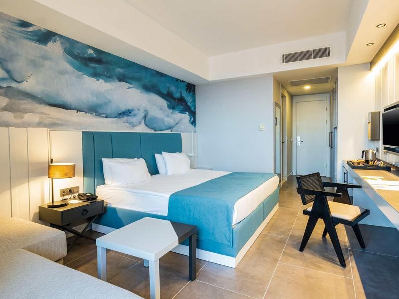 Habitación de hotel moderna con cama doble, cabecero azul, escritorio y decoración minimalista.