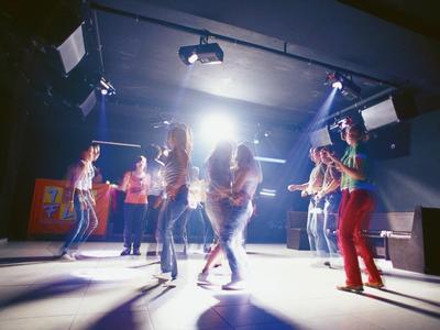 Gruppo di persone che ballano in una stanza buia con illuminazione intensa sul palco.