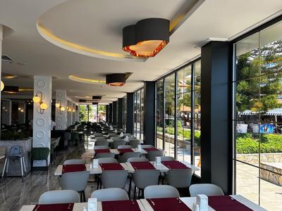 Modernes Restaurant mit langen Tischen, weißen Stühlen und großen Fenstern, rot-lila Tischläufer.