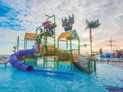 Buntes Wasserspielgerät mit Rutschen und Plattformen in einem Pool unter blauem Himmel.