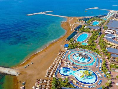 Küstenresort mit mehreren Pools, Sonnenschirmen und blauem Meer im Hintergrund an sonnigem Tag.