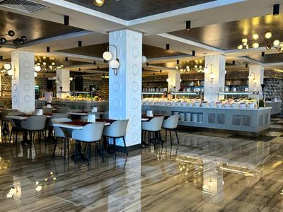 Modernes, elegantes Restaurant mit glänzendem Marmorboden, weißen Säulen und goldenen Kronleuchtern.