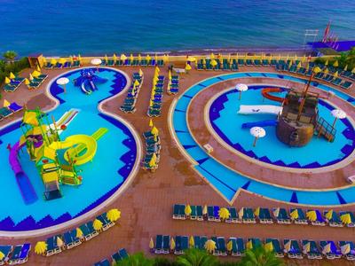 Großer Außenpool mit Rutschen und separatem Piratenschiff-Spielbereich am Meer, viele Liegen ringsum.