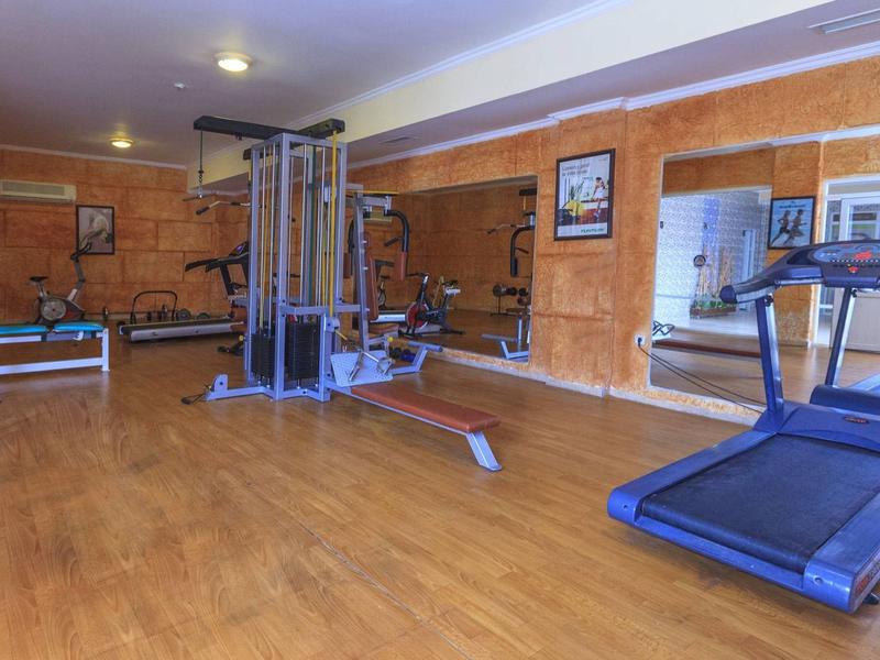 Innenraum eines Fitnessraums mit Laufband, Multifunktionsgerät und Hantelbänken, Holzwandverkleidung.