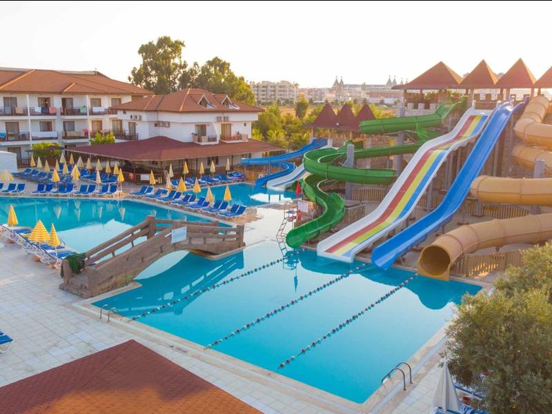 Großer Poolbereich mit Wasserrutschen, Sonnenliegen und Hotelgebäuden bei Sonnenuntergang.
