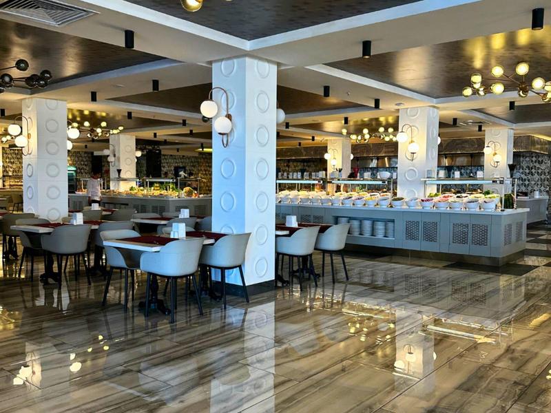 Modernes, elegantes Restaurant mit glänzendem Marmorboden, weißen Säulen und goldenen Kronleuchtern.